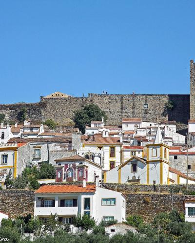 A view of a hilltop town with white houses and terracotta roofs, dominated by a large medieval stone castle with a prominent square keep and crenellated walls on the ridge above.