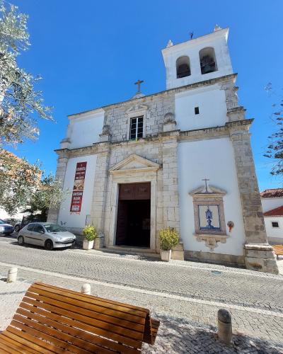 A low-angle photograph of a white church facade with a stone-trimmed entrance, a bell tower, and a red banner hanging on the left wall.