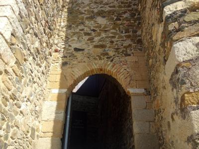 A view looking up through a narrow stone archway into a dark interior passage, with a sign visible inside reading "MUSEU DE MERTOLA O CASTELO".