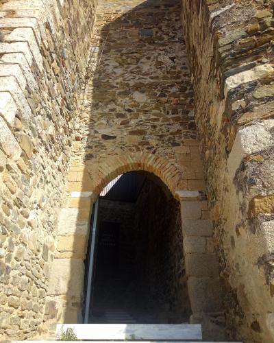A view looking up through a narrow stone archway into a dark interior passage, with a sign visible inside reading "MUSEU DE MERTOLA O CASTELO".