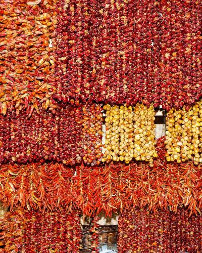 A close-up view of numerous strings of dried red and yellow chili peppers hanging in dense rows, likely within a market stall.