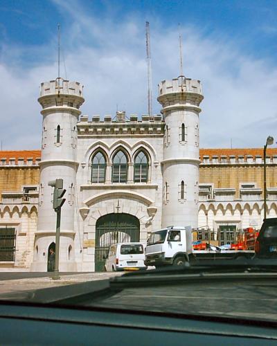 A large, castle-like stone building with two prominent round towers flanking a central arched gateway, viewed from a street with vehicles in the foreground.