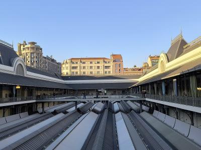 A wide-angle view of the interior courtyard of a large, historic market building featuring a distinctive metal and glass roof structure, upper-level walkways with railings, and a central area with escalators.
