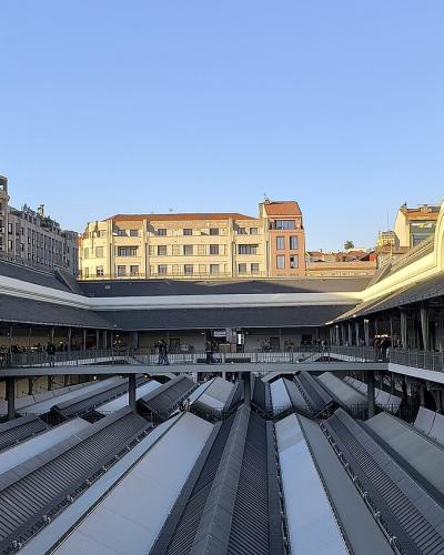 A wide-angle view of the interior courtyard of a large, historic market building featuring a distinctive metal and glass roof structure, upper-level walkways with railings, and a central area with escalators.