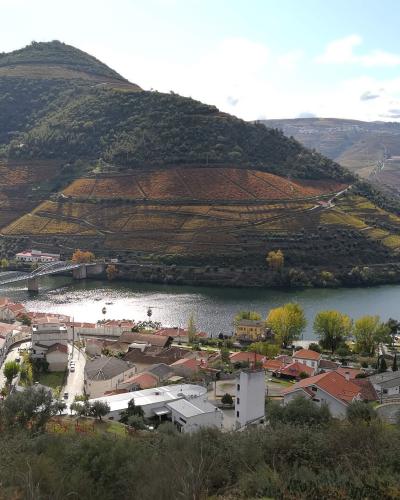 A high-angle landscape view of the village of Pinhão situated on the banks of the Douro River, featuring terraced vineyards on the hillsides and a prominent metal railway bridge crossing the water.