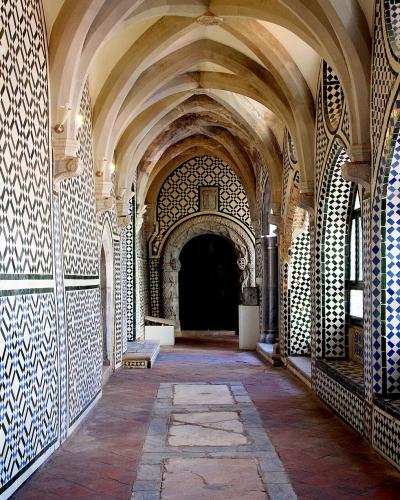 A long, vaulted corridor with Gothic-style ribbed ceilings and walls covered in intricate black, white, and blue geometric azulejo tilework, featuring arched windows on the right and a dark doorway at the far end.